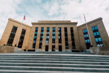 Fachada do edifício do Federal Reserve, vista de baixo, com bandeiras dos Estados Unidos e céu nublado.