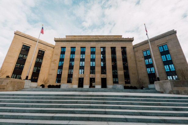 Fachada do edifício do Federal Reserve, vista de baixo, com bandeiras dos Estados Unidos e céu nublado.