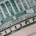 Cédula de dez dólares e edifício do Tesouro dos Estados Unidos sobre uma mesa.