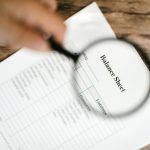 Balanço financeiro sob uma lupa sobre uma mesa de madeira.