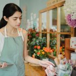 Empreendedora consulta um tablet em uma floricultura enquanto organiza um pedido.