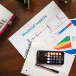 Relatórios financeiros com gráficos e uma calculadora sobre uma mesa, representando análise de indicadores econômicos.