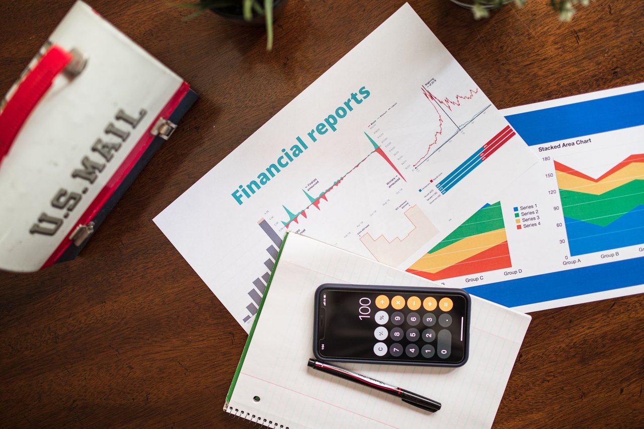 Relatórios financeiros com gráficos e uma calculadora sobre uma mesa, representando análise de indicadores econômicos.