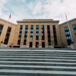 Vista externa do edifício do Federal Reserve em Washington, com bandeiras dos Estados Unidos e escadaria.