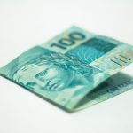 Close de uma cédula brasileira de 100 reais sobre uma superfície neutra.