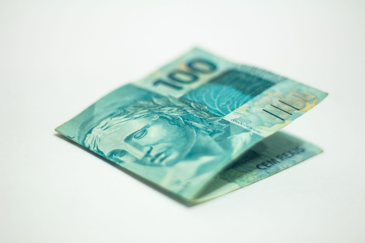 Close de uma cédula brasileira de 100 reais sobre uma superfície neutra.