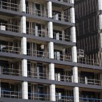 Edifício residencial em construção, com andaimes e trabalhadores em uma área urbana.