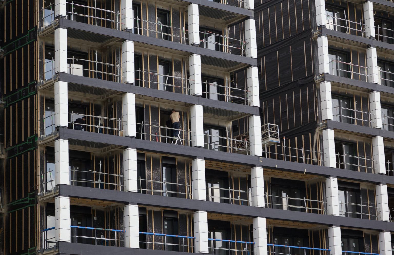 Edifício residencial em construção, com andaimes e trabalhadores em uma área urbana.