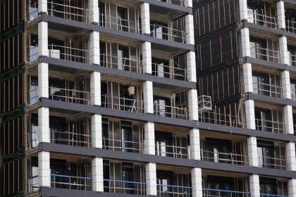 Edifício residencial em construção, com andaimes e trabalhadores em uma área urbana.
